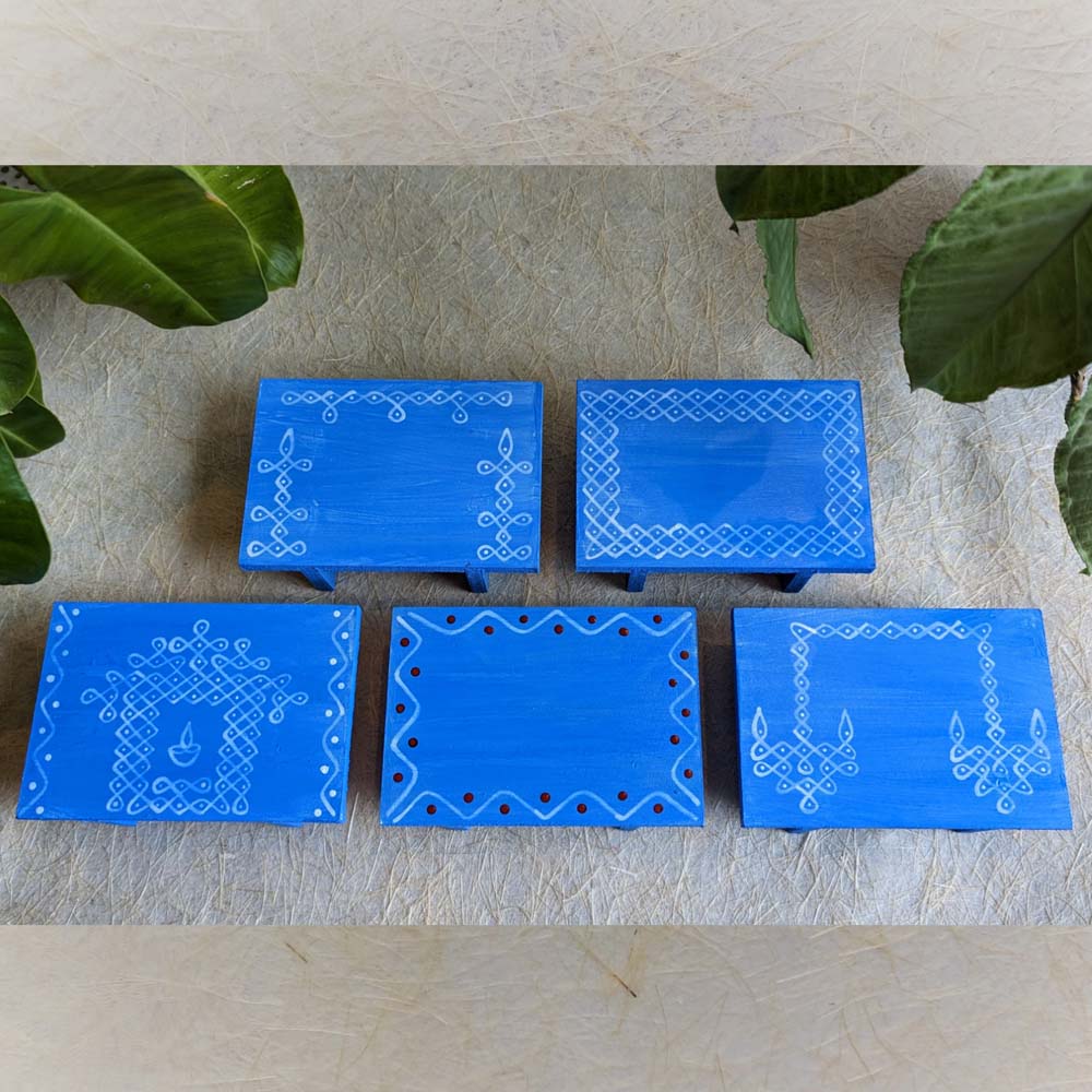 Blue wooden pooja platform with intricate white Kolam patterns, perfect for rituals and decor.