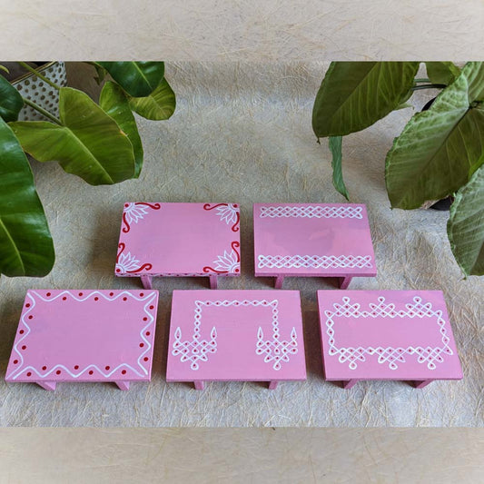 Pink wooden pooja platform with intricate white Kolam patterns, perfect for rituals and decor.