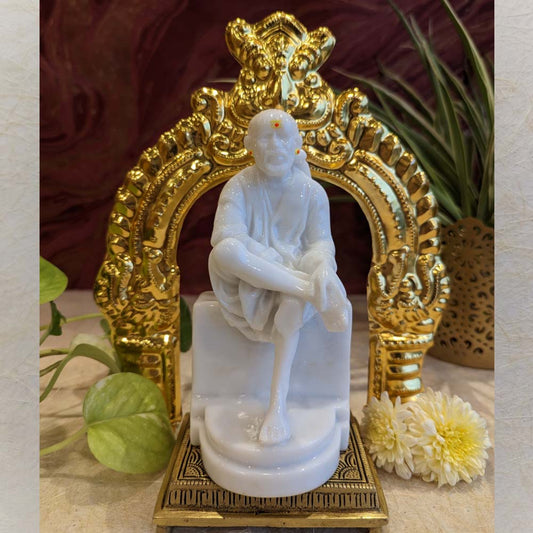 Ornate golden brass Thiruvachi with intricate carvings, placed on a tabletop surrounded by flowers and plants.