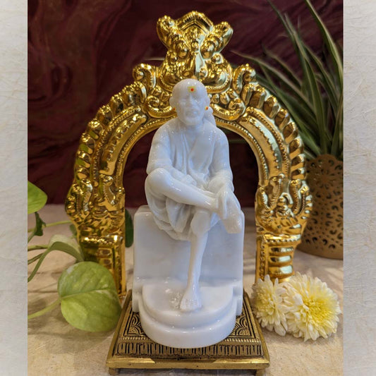 Ornate golden brass Thiruvachi with intricate carvings, placed on a tabletop surrounded by flowers and plants.