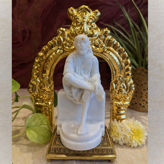 Ornate golden brass Thiruvachi with intricate carvings, placed on a tabletop surrounded by flowers and plants.