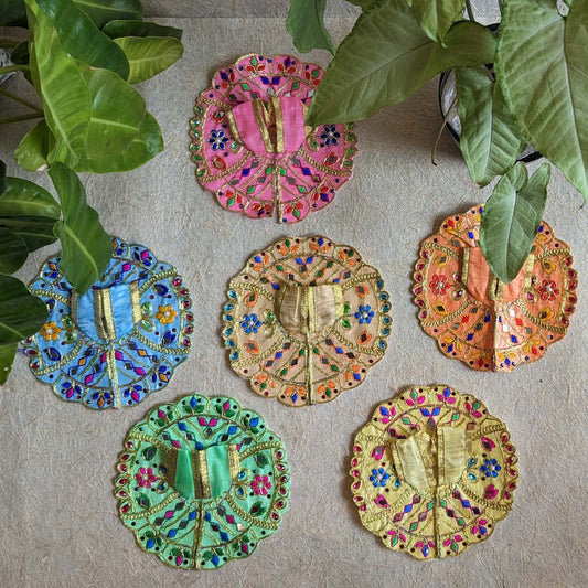 A set of six traditional Lalji Vastras in vibrant colors with intricate embroidery and mirror work, placed on a textured surface with green leaves around.