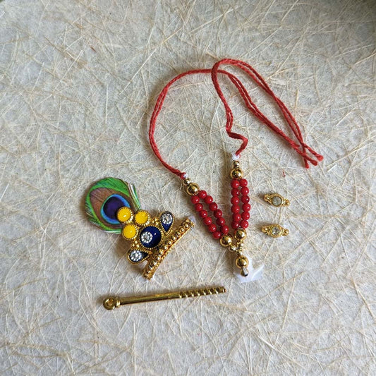 Traditional Krishna ornament set with a peacock-feather crown, red beaded necklace, flute, and decorative earrings for deity decoration.