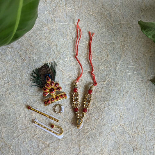 A Krishna ornament set featuring a peacock feather crown, earrings, necklace, and accessories, intricately designed with red beads and golden embellishments.
