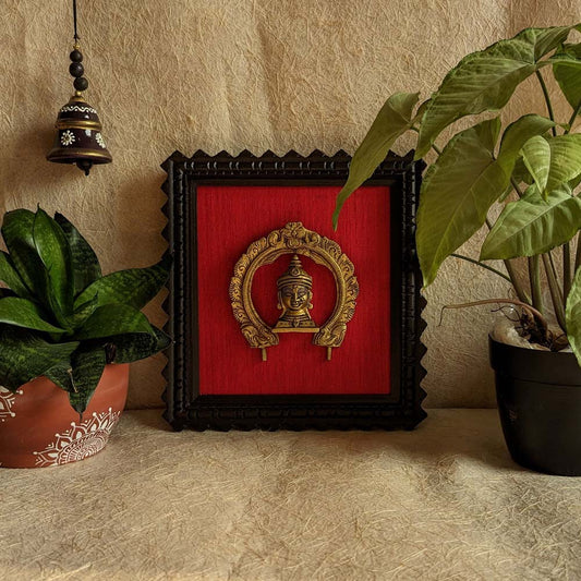Brass Goddess Gauri wall décor with ornate arch mounted on red velvet background in a black wooden frame.