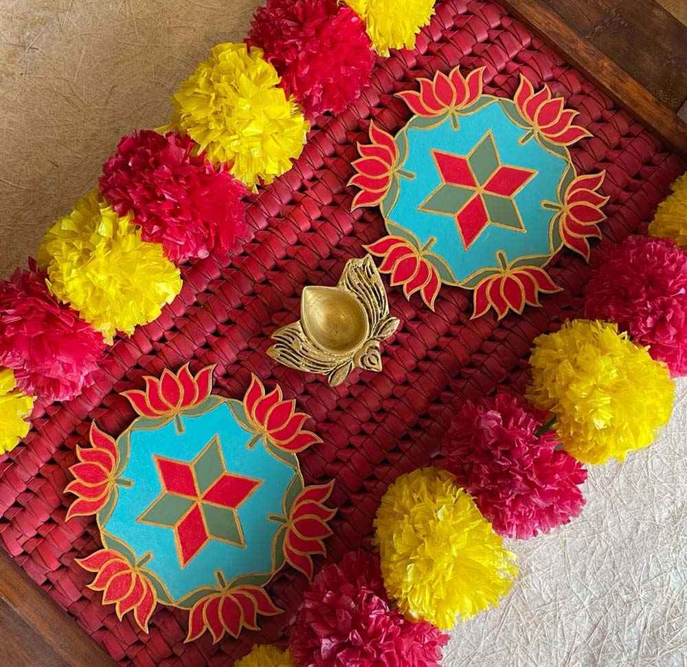 Set of 2 handcrafted decorative Lotus Rangolis with turquoise bases and red and gold lotus designs, surrounded by yellow and red floral garlands.
