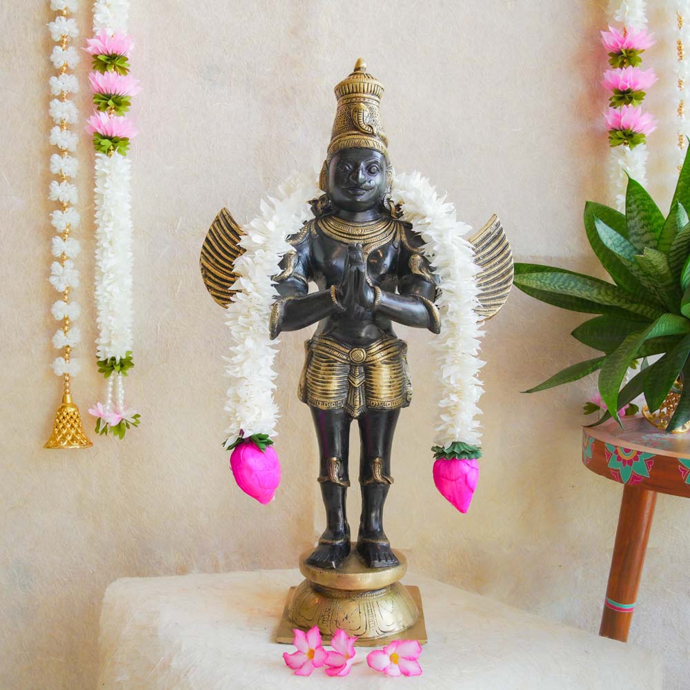 Handcrafted brass Garuda statue with intricate detailing, adorned with floral garlands and displayed with traditional decor.